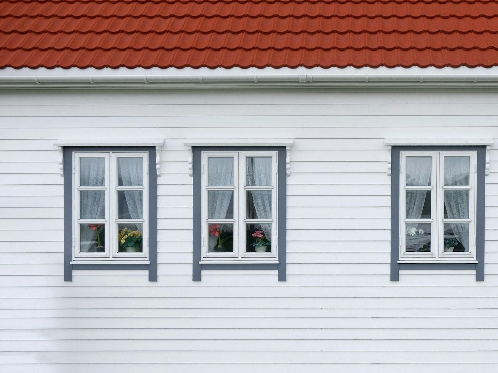 White lap siding with three gray-trimmed windows in straight, even courses under a terracotta tile roof, in soft overcast light.