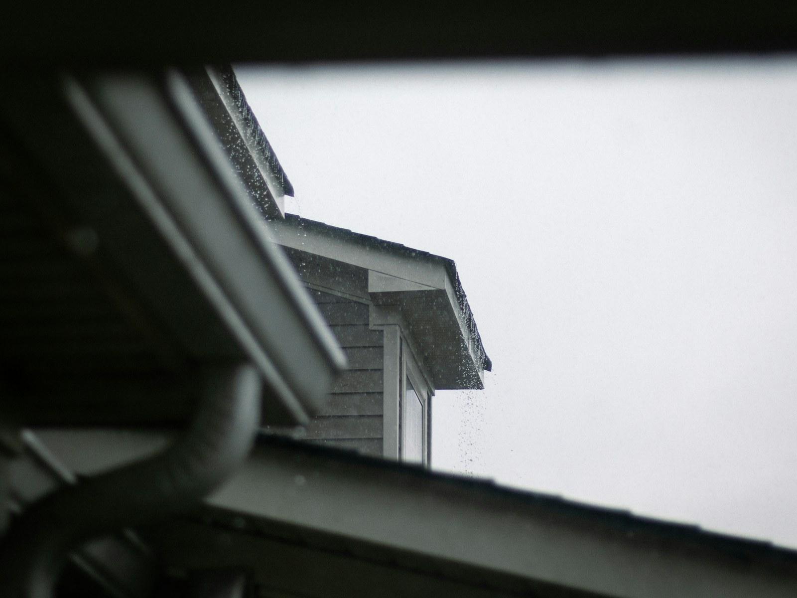 Gutter and downspout corner under a roof edge against an overcast sky.