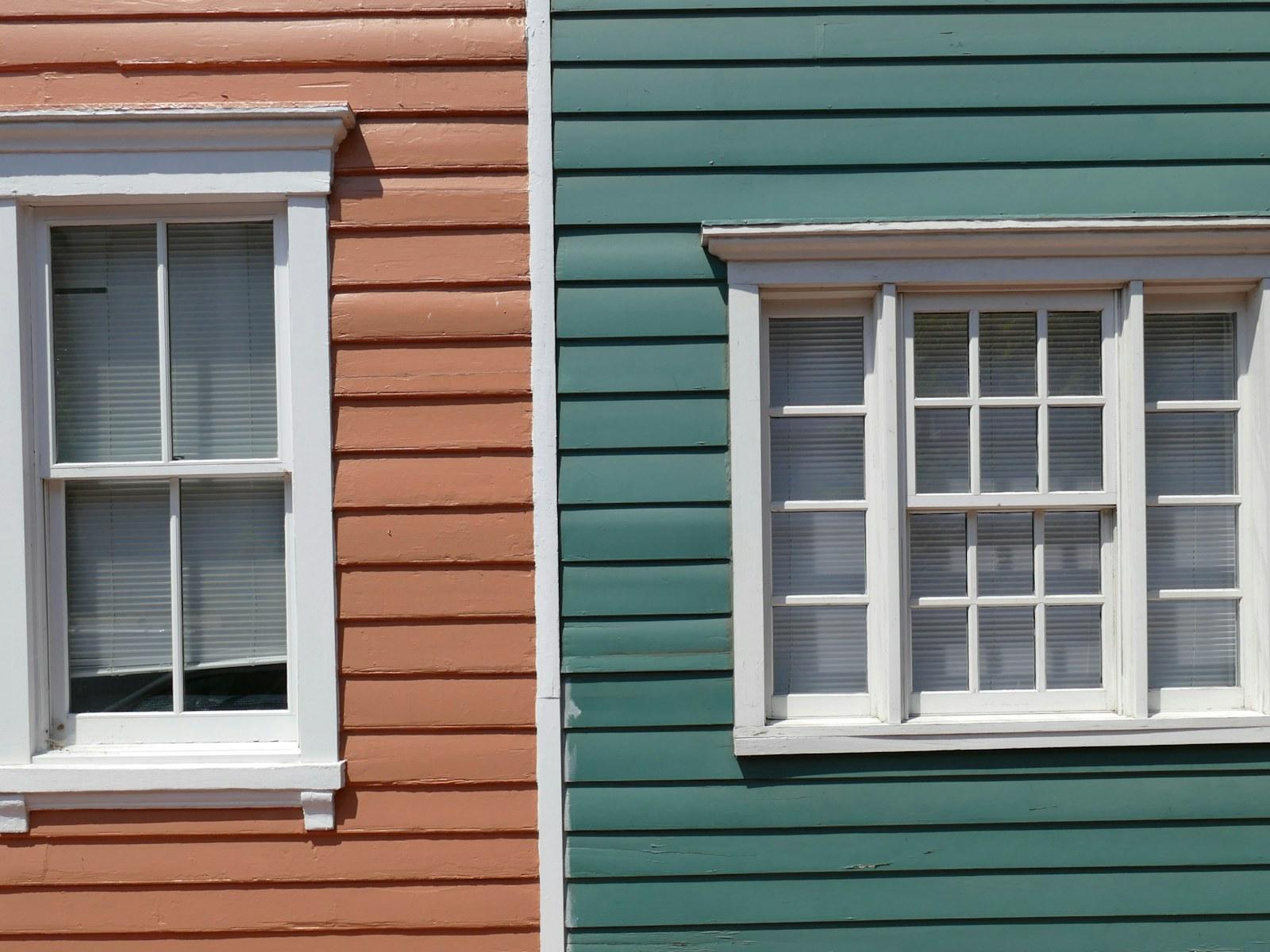 Two windows with fresh white trim on lap siding, one wall painted terracotta and the other green.