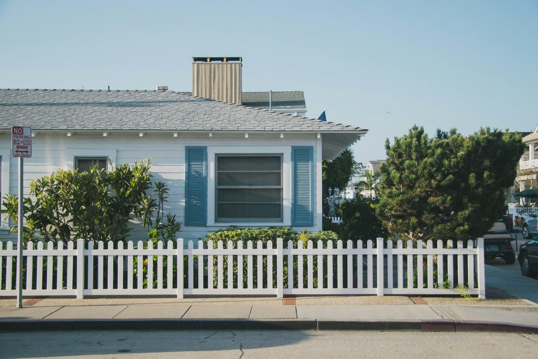 White single-story home with blue shutters and a white picket fence after exterior work.